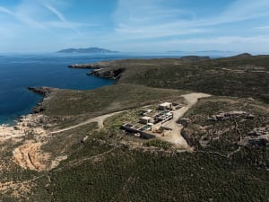 Aerial view of a modern concrete villa built on a rocky cliff overlooking the deep blue Mediterranean sea under a clear sky.
