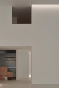 Modern minimalist entryway featuring warm wooden cabinetry, textured concrete wall with integrated lighting, and clean white architectural volumes.