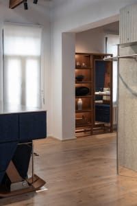 Modern minimalist entryway featuring a blue upholstered bench with walnut base, built-in walnut display shelves with decorative objects, light wood flooring, and a textured beige wall panel.