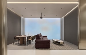 Modern minimalist living and dining room featuring a brown leather modular sofa, light wood and marble dining table with beige chairs, and a large blue gradient accent wall.