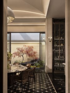 Modern luxury dining room with round marble table, velvet dining chairs, black and white patterned marble floor, and a Japanese maple tree in an indoor courtyard visible through large glass doors.