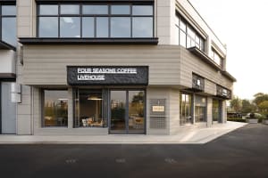 Modern corner commercial building with horizontal travertine stone cladding, large glass windows, and black textured signage for Four Seasons Coffee Livehouse.
