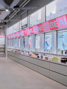 Long minimalist retail display wall in a modern beauty store with grey cabinetry, backlit product niches, and large pink signage reading MUSINSA BEAUTY.