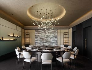 Luxurious private dining room featuring a large circular black marble table with lazy Susan, eight white upholstered dining chairs, dramatic modern starburst chandelier, and a large Chinese landscape mural on the back wall.