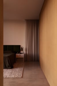 Modern minimalist bedroom featuring a dark green velvet headboard, walnut wood wall paneling, concrete floor, and neutral-toned curtains.