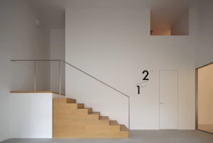 Modern minimalist interior featuring a light oak floating staircase against clean white walls with geometric lines and recessed lighting.