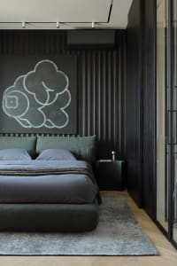 Modern dark-toned bedroom with sage green upholstered bed, large cloud-shaped artwork in teal on black wall, wood herringbone floor and grey area rug.