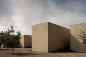 Modern minimalist rammed earth architectural volumes in a desert landscape with olive trees and dramatic cloudy sky
