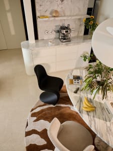 Modern breakfast nook featuring a curved Calacatta marble table, a sculptural black organic chair, a cowhide rug, and a built-in marble coffee station with espresso machine.