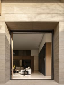 View through a large travertine stone doorway into a modern minimalist living room with neutral furnishings and dark wood accents