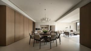 Modern minimalist dining room featuring a round dark marble table, six light grey upholstered chairs, a large white sculptural chandelier, and full-height oak cabinetry that flows into an open living room in the background.