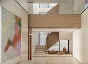 Modern minimalist double-height foyer with a curved oak staircase, large colorful abstract painting, stone sculptures, and high windows allowing natural light.