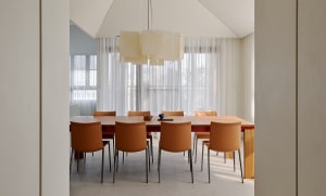 Modern minimalist dining room featuring a long light oak dining table, six burnt orange leather chairs, and a large geometric fabric pendant light hanging above.