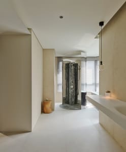 Modern minimalist bathroom with beige textured walls, white floor tiles, a dramatic dark marble open shower, floating white vanity, and a natural wood stump stool.