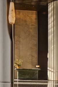 Elegant luxury hotel lobby featuring a carved green marble reception desk, a large bronze wall with traditional Chinese mountain landscape, hanging marble pendant light, and patterned marble floor.
