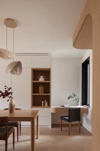 Modern minimalist dining area with light oak table and chairs, built-in wooden study desk and shelving unit, beige pendant lights, and neutral color palette.