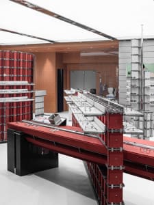 Modern optical store interior with bold red lacquered display counters and shelving units filled with eyeglasses under bright ceiling lighting.