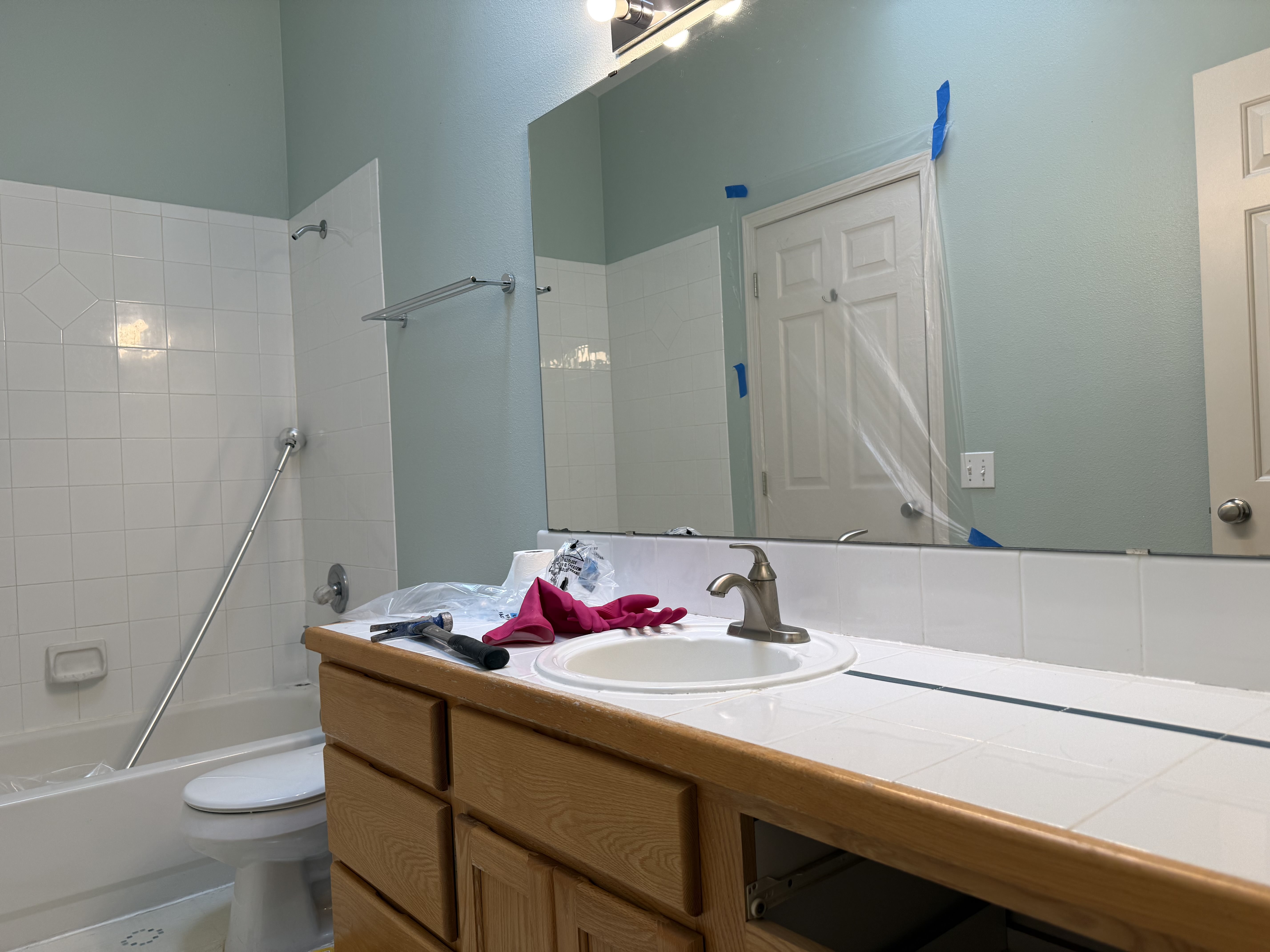 Before detail: tiled countertop with oak edge; grab bar in tub; tools staged for demo