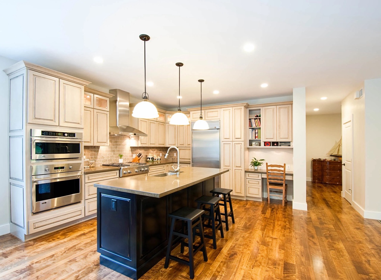Brightly lit modern kitchen with marble tops and large island with sink and stools for seating