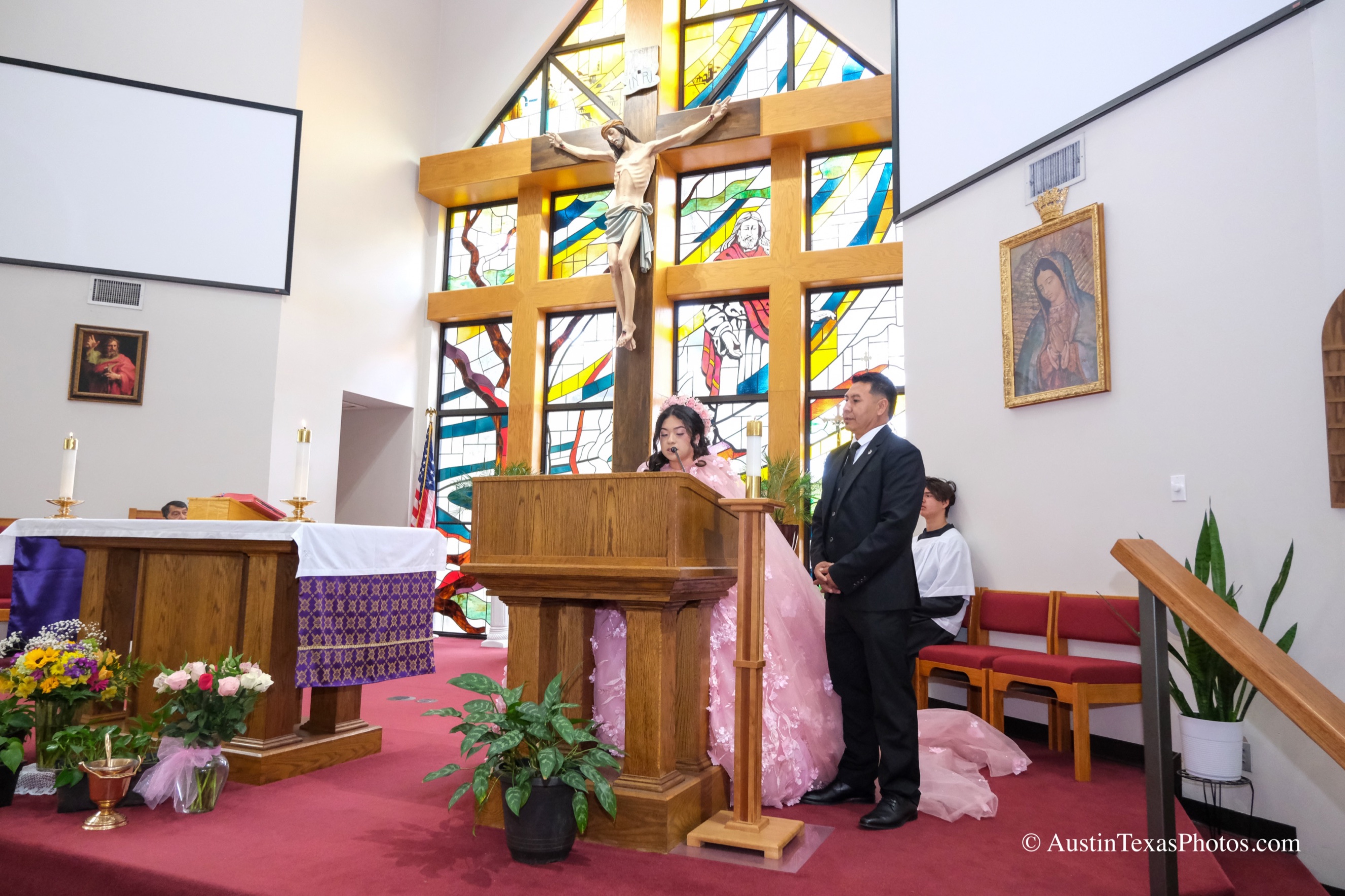 Quinceañera in pink gown at the altar lectern during mass at St. Paul Catholic Church, Austin, Texas, with crucifix and stained glass behind her