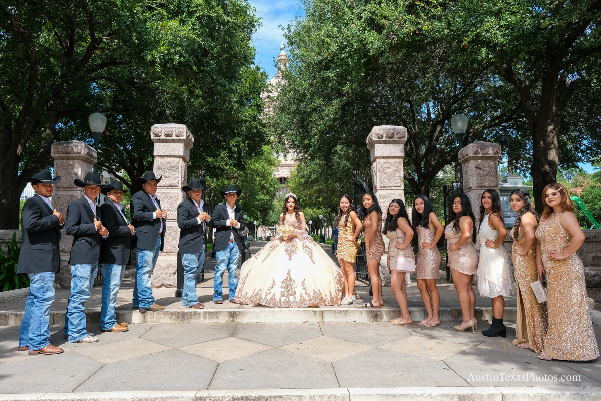 Quinceañera in champagne gown with full court of damas and chambelanes at the Texas State Capitol gates, Austin, Texas, with the dome visible behind the group