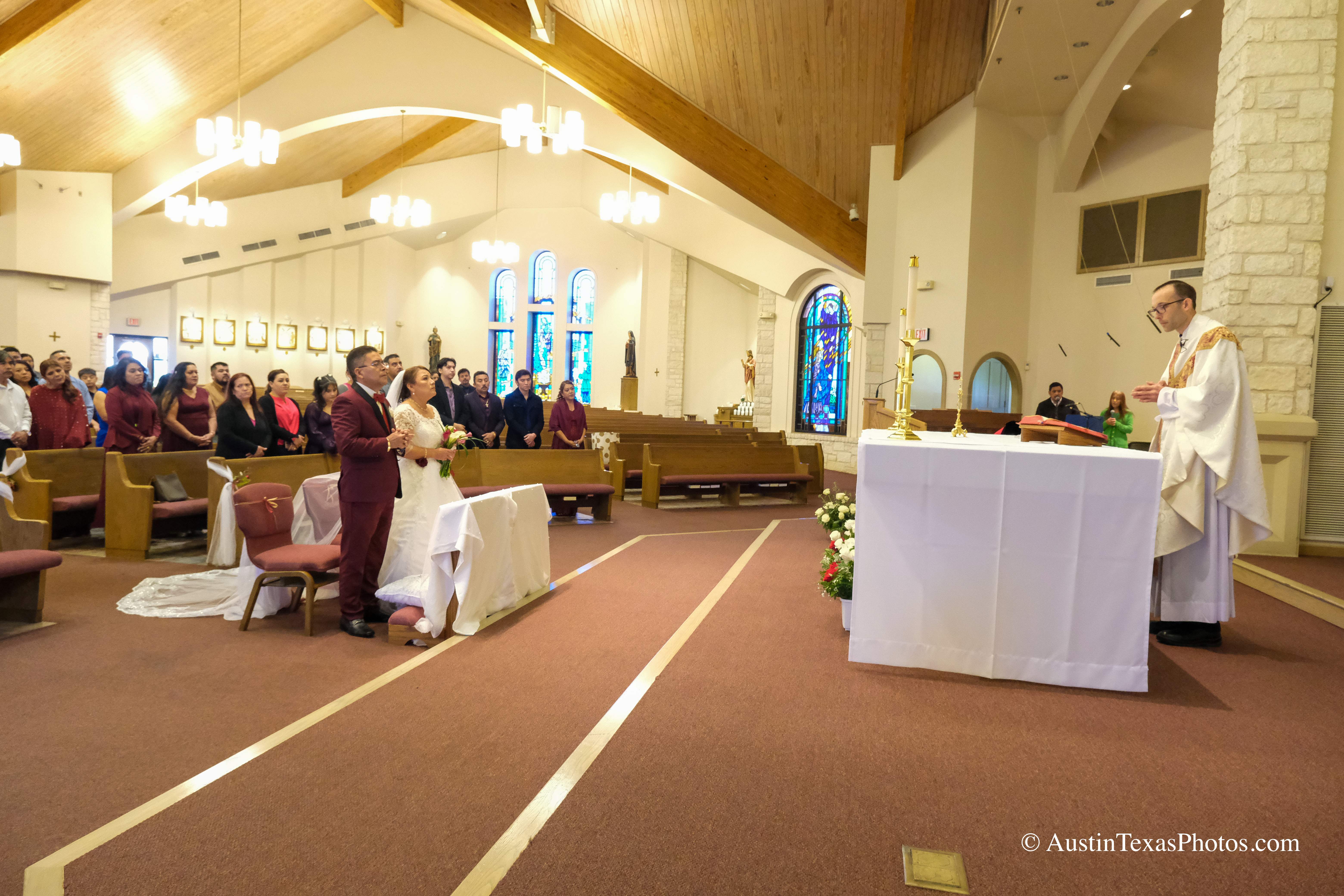 Bride and groom with priest at Santa Cruz Catholic Church wedding ceremony in Buda, Texas