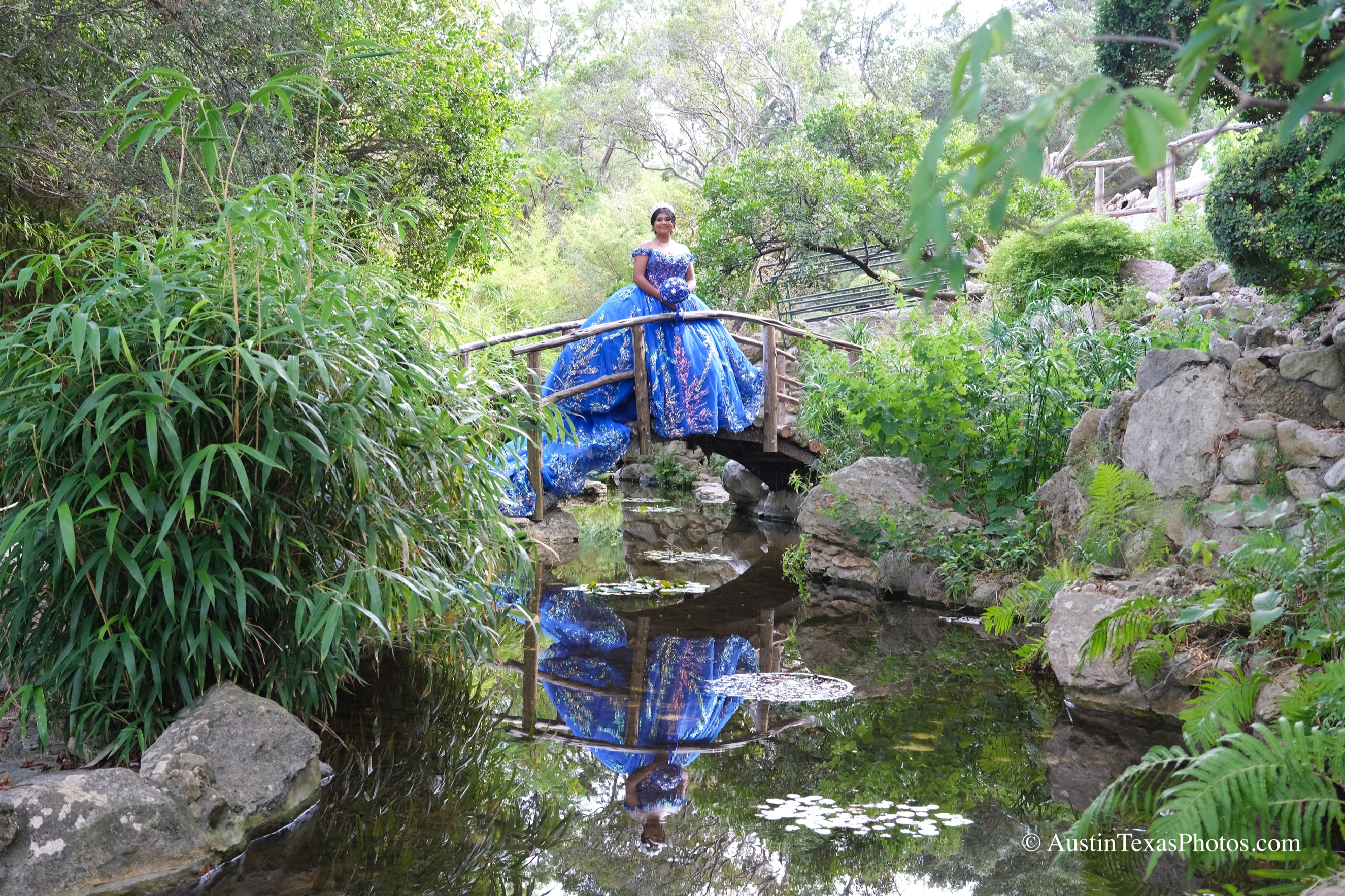Quinceañera in royal blue gown on a wooden bridge over a koi pond at Zilker Botanical Garden, Austin, Texas