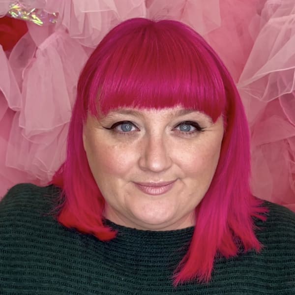 close up of Ruth Jones head & shoulders, standing in front of pink installation in her studio