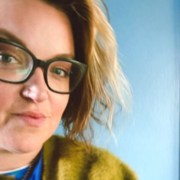 Steph Baker standing against blue wall in green