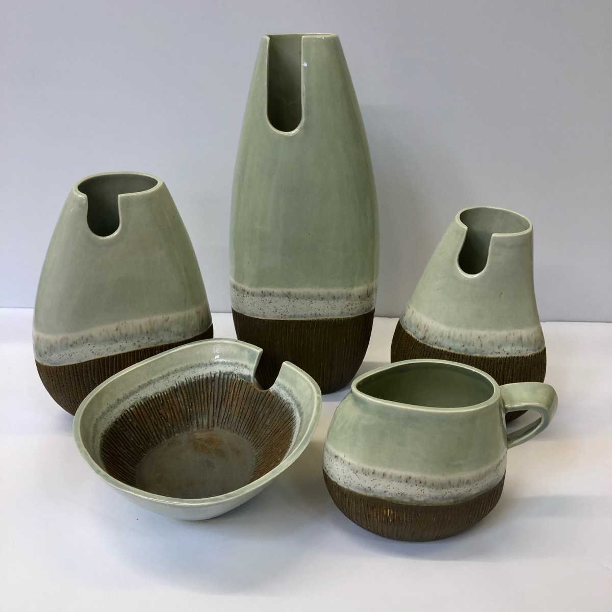 A collection of ceramic domestic forms in tri colour glazed soft green and earth tones. 