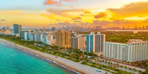 Miami Beach coastline at sunset with turquoise ocean, sandy beach, and downtown skyline hotels and high-rises