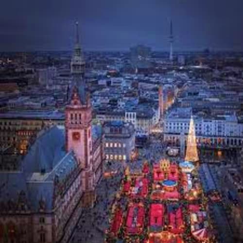 Aerial view of Hamburg city center at dusk with Christmas market below historic church spire and lit buildings