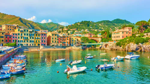 Colorful waterfront village in Liguria with moored boats and terraced hillside houses overlooking turquoise Mediterranean wat