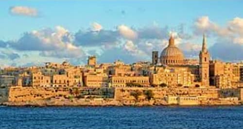 Valletta skyline with golden-lit historic buildings, dome and spires along Mediterranean waterfront