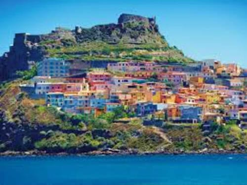 Colorful village of Castelsardo on Sardinian coastline with castle ruins on hilltop overlooking blue Mediterranean Sea