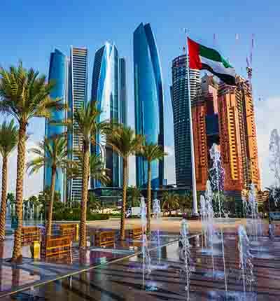 Abu Dhabi skyline with modern skyscrapers, UAE flag, palm trees, and fountain plaza with clear blue sky