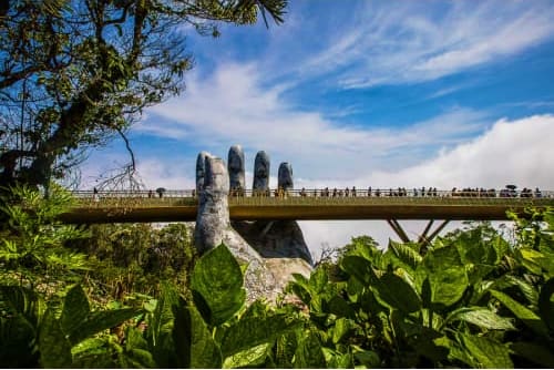 Golden Bridge with giant stone hands in Da Nang, Vietnam, surrounded by lush greenery and blue sky