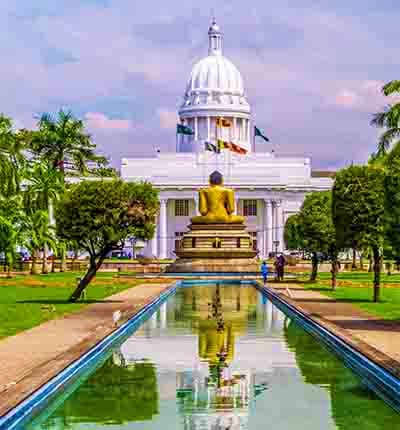 Golden Buddha statue with reflecting pool in front of white-domed parliament building surrounded by green grounds in Colombo