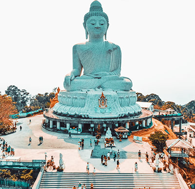Giant turquoise Buddha statue seated on elevated platform with visitors and stairs at base in Phuket, Thailand