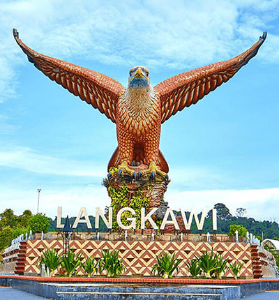 Large golden eagle monument with outstretched wings above Langkawi sign and ornamental base against blue sky