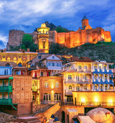 Tbilisi old town at dusk with colorful buildings and illuminated Narikala Fortress on the hill above