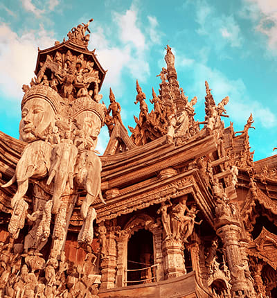 Ornate wooden temple facade with intricate carved details and pointed spires against blue sky in Pattaya, Thailand