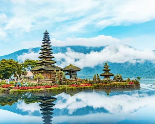 Pura Ulun Danu temple reflected in calm lake water with mountains and mist in background, Bali