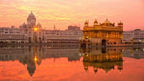 Golden Temple illuminated at sunset reflected in still water, Amritsar's sacred Sikh shrine with ornate domes and architectur