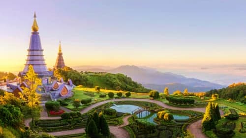 Phra Mahathat Napamatanidol temple with golden spires at sunrise overlooking mountains and manicured gardens in Chiang Mai, T