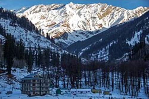 Snow-covered Himalayan mountain valley with coniferous forest and traditional building in Manali during winter