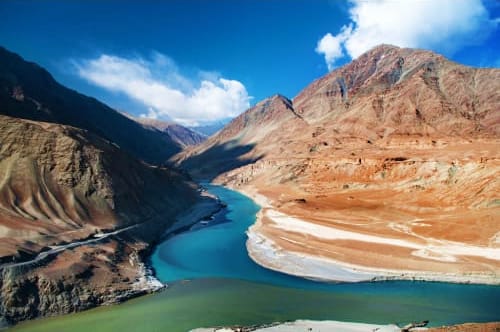Confluence of turquoise and green rivers at the base of barren mountains in Leh, Ladakh, India