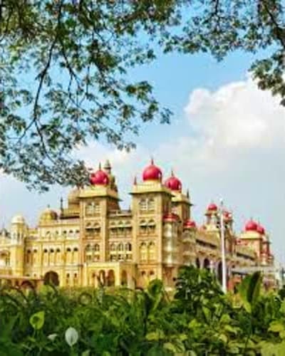 Mysore Palace with distinctive red domes and golden architecture viewed through tree branches under blue sky