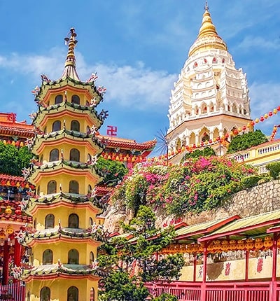 Penang Buddhist temple with golden and white pagodas, pink bougainvillea flowers, and traditional red temple structures under