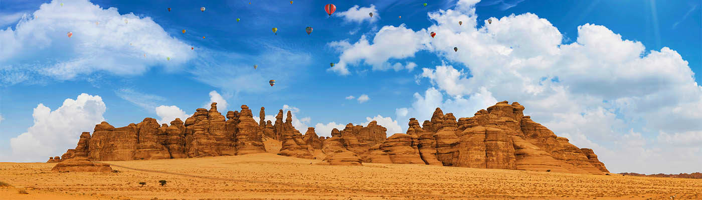 Hot air balloons floating over rocky desert landscape and sandstone formations in Al Ula, Saudi Arabia